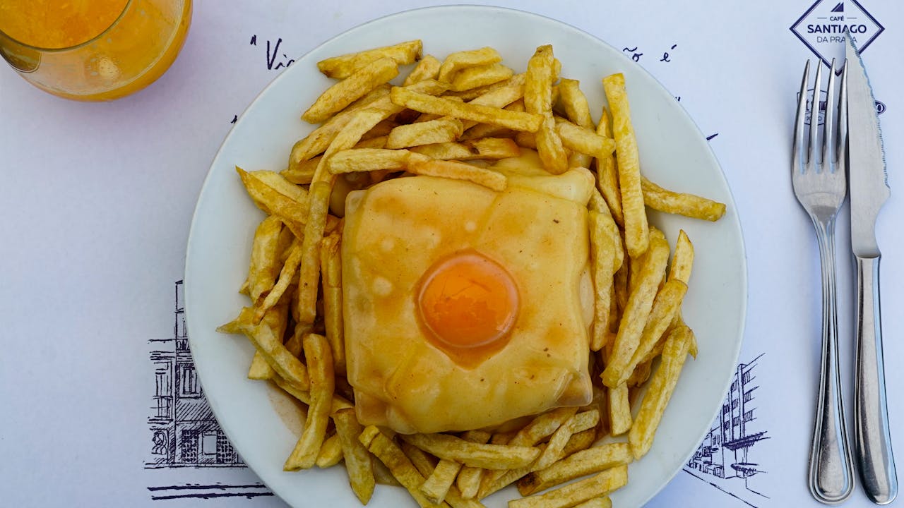 about-01 Tasty Portuguese francesinha sandwich topped with egg, surrounded by crispy fries and fresh juice.