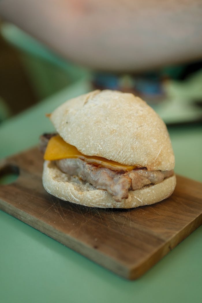 gallery-5 Close-up of a homemade burger with cheese on a wooden cutting board, ideal for food enthusiasts.