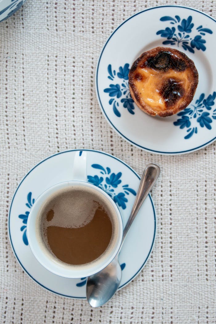 services-01 Top view of a Portuguese egg tart and coffee on a floral ceramic plate, showcasing a warm and cozy breakfast scene.